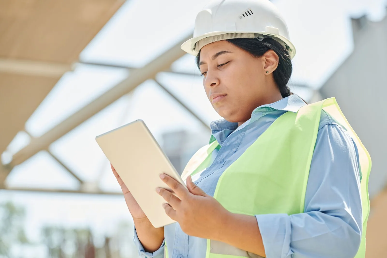 Handwerkerin mit Schutzhelm und Warnweste liest auf einem Tablet auf der Baustelle